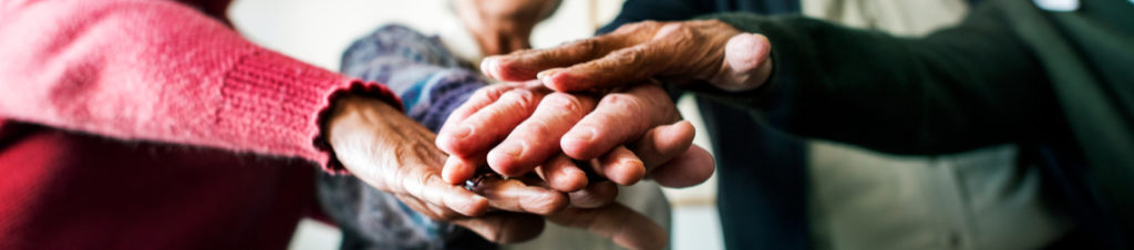 Elderly hands stacked in unison, representing community