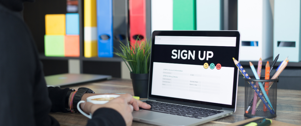 Laptop on a desk with an open screen that says "SIGN UP" in big white letters.