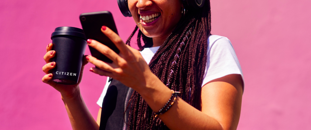 A woman listening to music on her phone against a bright pink backdrop.