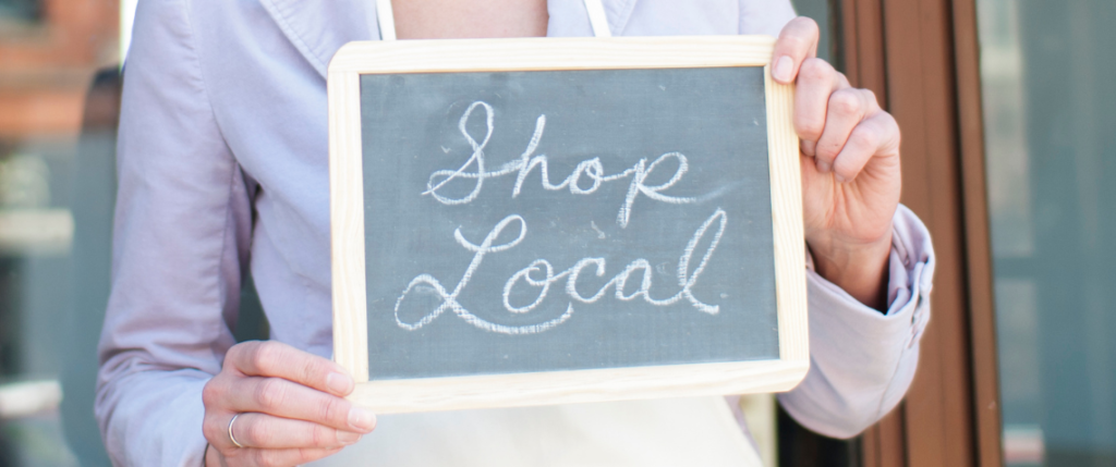 Woman holding small chalkboard with the words "Shop Local" scrawled in cursive in white chalk.